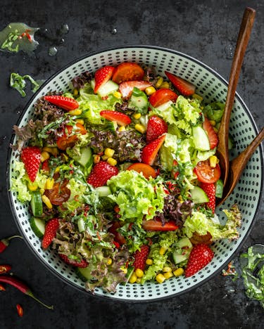 Eine große Salatschüssel, gefüllt mit einer farbenfrohen grün-roten Salatmischung, ist von oben auf anthrazitfarbenem Hintergrund abgebildet.