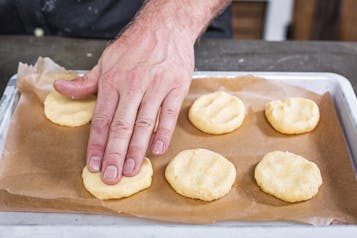 Parmesan-Cookies werden mit der Hand auf einem Backblech angedrückt