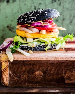 Schwarzfarbener Burger mit Salat, Zweibeln, Spargel und Polenta auf einem Holzbrett