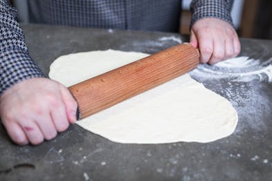 Pizzateig wird mit einem Nudelholz ausgerollt