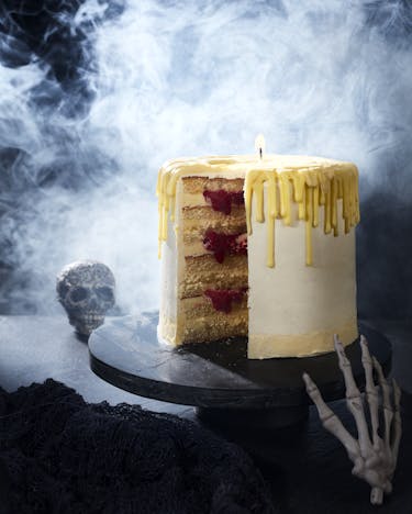aufgeschnittene Torte in Form einer Kerze auf dunkler Tortenplatte mit rauchendem Totenkopf im Hintergrund