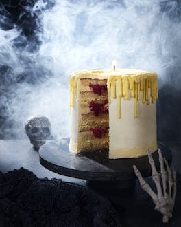 aufgeschnittene Torte in Form einer Kerze auf dunkler Tortenplatte mit rauchendem Totenkopf im Hintergrund