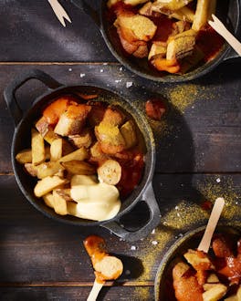 Currywurst mit Pommes in kleinen schwarzen Pfännchen