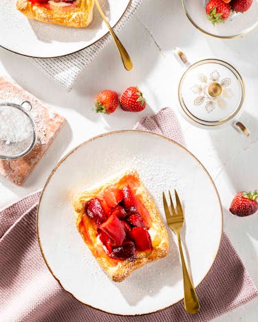 Vanille-Erdbeer-Plunder auf einer hellen gedeckten Kaffeetafel. Eine goldene Gabel liegt daneben.