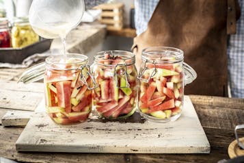 Drei Einmachgläser mit Wassermelonen werden mit süß-saurer Einlegeflüssigkeit begossen