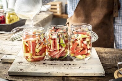 Drei Einmachgläser mit Wassermelonen werden mit süß-saurer Einlegeflüssigkeit begossen
