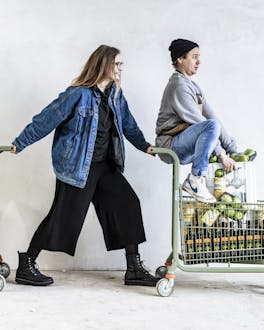 Food Editorin Leonie und Foodstylist Hannes gehen Vorräte mit ihren Einkaufswagen shoppen.