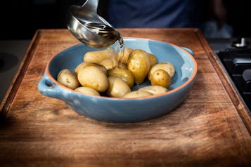 Gekochte ungeschälte Kartoffeln in einer hellblauen Form werden mit einer Kelle mit Wasser übergossen