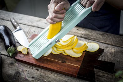 Eine gelbe Zucchini wird mithilfe einer Reibe in dünne Scheiben geraspelt