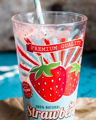Buntes Glas mit Erdbeer-Druck neben Flasche mit Erdbeer-Smoothie auf blauem Untergrund