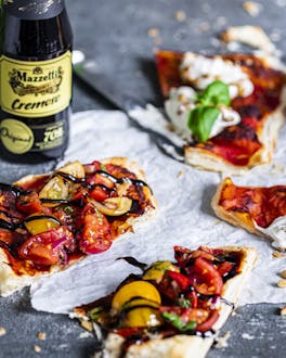 Blätterteig-Pizzette mit Tomaten und Ricotta, daneben eine Flasche Mazzetti Cremoso