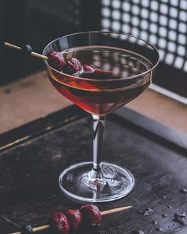 Klassischer Manhattan Cocktail mit Whisky und Wermut in einer Cocktailschale mit Kirschen auf einem Holzspieß.