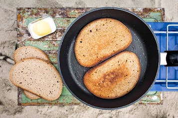 In einer Pfanne liegen 2 Scheiben Brot. Danebenliegen weitere 2 Scheiben Brot und eine Schale mi Butter.