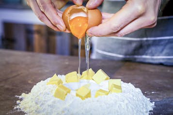 Butterwürfel auf Mehlhaufen und Hände, die Ei dazugeben