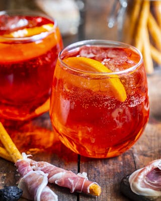 Zwei leuchtend rote Drinks mit Orangenscheibe in Gläsern auf Holzuntergrund