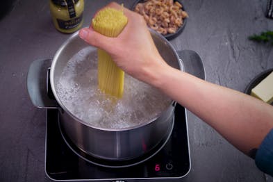 Mit einer Hand werden rohe Spaghetti in einen Topf voll kochendem Wasser gegeben.