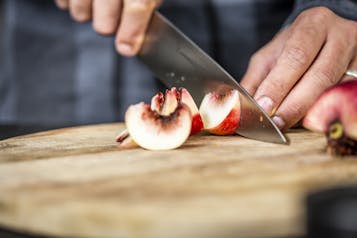 Ein Pfirsich wird auf einem Holzbrett mit einem Messer geachtelt