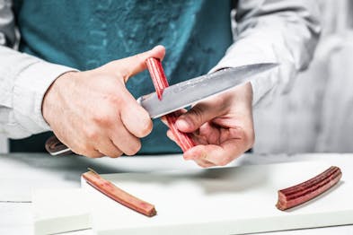 Eine Rhabarberstange wird mit einem Messer eingeritzt.
