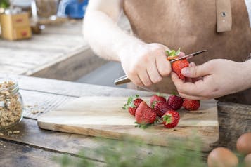 Von Erdbeeren auf einem Holzbrett wird das Grün mit einem Messer entfernt