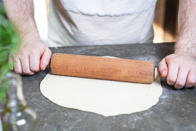 Pizzateig für Pizza Prosciutto wird mit Nudelholz ausgerollt