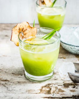 Green delight drink mit Eiswürfeln im Glas mit Apfelchips am Glasrand auf Holzuntergrund.