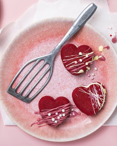 Herz-Whoopies aus Red Velvet Teig mit heller Creme vor rosa Hintergrund