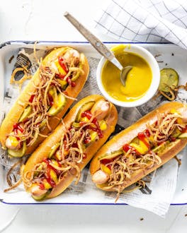 Drei klassische Hot Dogs in weißer Schale angerichtet auf weißem Untergrund