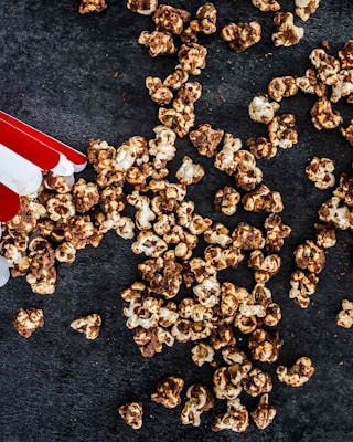 Popcorn mit Erdnussbutter und Karamell in gestreiften Popcorntüten auf dunklem Untergrund