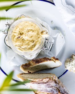 Einmachglas mit Dattel-Frischkäse-Dip  und Baguette auf weißem Teller.