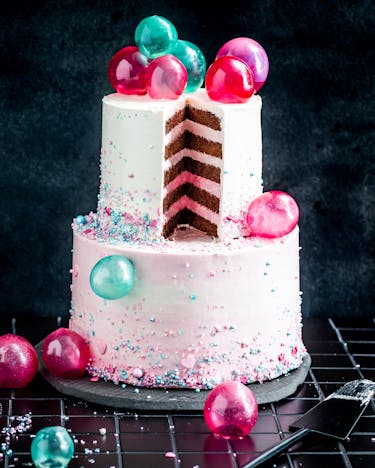 Angeschnittener Bubble Cake mit pinken und türkisen Gelatine-Kugeln vor schwarzem Hintergrund