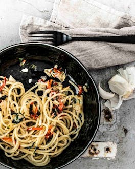 Spaghetti aglio e olio auf schwarzem Teller und grauem Hintergrund