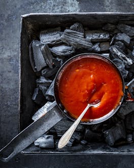 Rote BBQ-Sauce in gusseisernen Schalen auf schwarzer Kohle.
