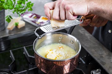 Parmesan wird mit einer Reibe in einen Topf Risotto gerieben