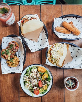 Quelle: Pay Now Eat Later. Das Restaurant Macaibo in Hamburg, man sieht einen Holztisch von oben mit vielen Leckereien von Tacos über Salat bis leckere Drinks.