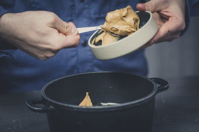 Erdnussbutter wird mit einem Löffel aus einer Schüssel in einen Topf gegeben