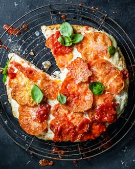 Angeschnittene Fladenbrot-Pizza, die mit Ochsenherztomaten, Burrata, Parmesan und frischem Basilikum belegt ist