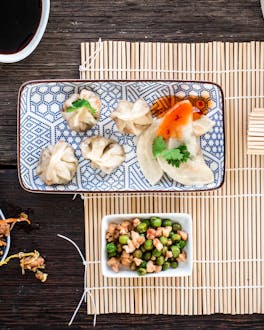 Gefüllte chinesische Dumplings auf einem flachen Teller und Bambusmatten serviert neben Essstäbchen und einem Dämpfkorb