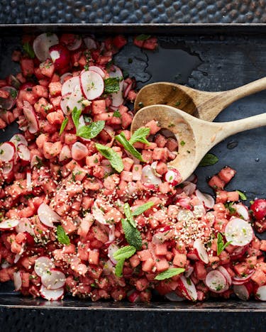Schwarzes Backblech mit rotem Wassermelonen-Radieschen-Salat und Holzlöffeln.