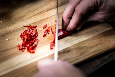 rote Chili wird auf einem Holzbrett mit einem großen Messer geschnitten