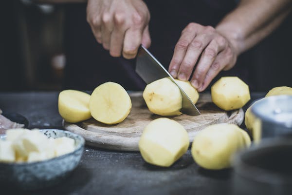 Mehrere Kartoffeln, die gerade mit einem Messer halbiert werden