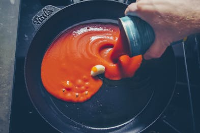 Passierte Tomaten werden in einer schwarze Pfanne mit Knoblauch gegeben