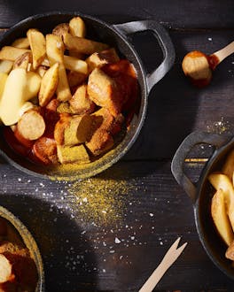 Currywurst mit Pommes in kleinen schwarzen Pfännchen
