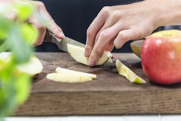 Holzbrett auf dem zwei Hände einen Apfel in Spalten schneiden