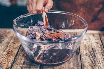 Rotkohlsalat wird von einer Hand mit einem schmalen Holzlöffel mit getrockneten Gewürzen gewürzt