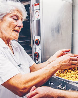 Ältere Frau in weißer Kleidung in Küche mit selbstgemachten Tortellini in Händen