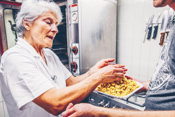 Ältere Frau in weißer Kleidung in Küche mit selbstgemachten Tortellini in Händen