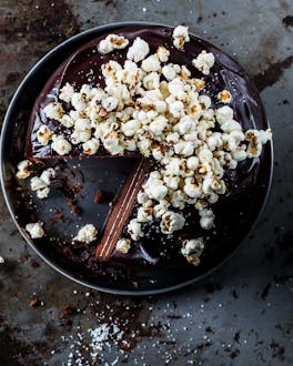 Angeschnittener Schokoladenkuchen mit Popcorn-Topping auf dunkler Servierplatte und Metalluntergrund.
