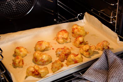 Auf einem Blech im Ofen sind Blumenkohlröschen mit BBQ-Sauce bestirchen.