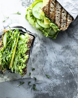 Vollkorn Sandwich großzügig belegt mit Avocadocreme, Salat, Gurke und Kresse auf grauer Marmorplatte