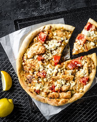 Pfannen-Pizza Bianca mit Hähnchen und Tandoori-Gewürz, von oben fotografiert auf dunklem Untergrund, ein Stück ist aus der Pizza bereits servierfertig geschnitten.